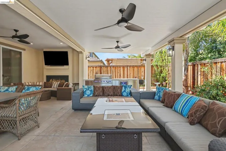 Fenced backyard featuring ceiling fan, a patio, exterior fireplace, and an outdoor kitchen with living area