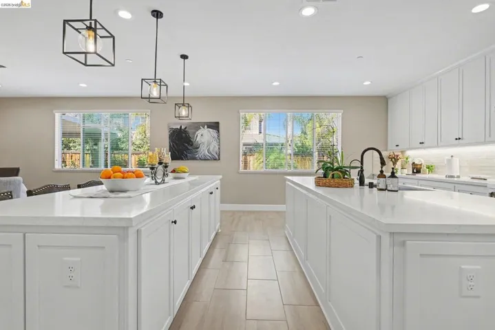 Kitchen with a spacious island, white cabinetry, light stone counters, decorative light fixtures, and decorative backsplash
