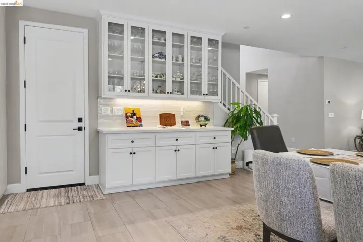 Bar featuring white cabinetry, glass fronted cabinets, backsplash, wood tiled floors, and light stone counters