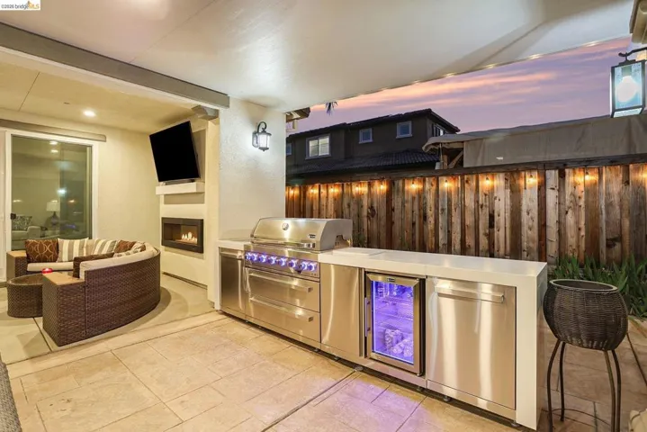 View of patio / terrace featuring a warm lit fireplace, exterior kitchen, and beverage cooler