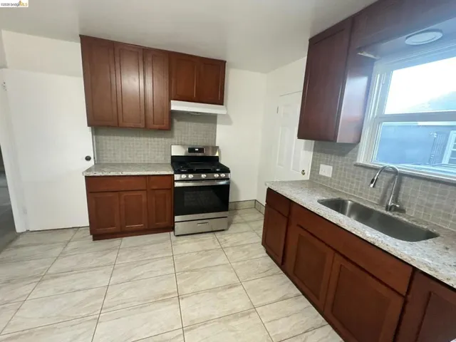 Kitchen featuring stainless steel gas range oven, backsplash, light stone counters, and light tile patterned floors