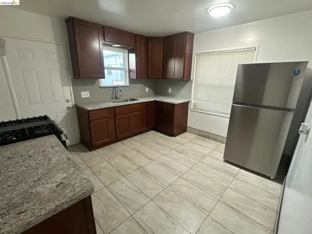 Kitchen featuring freestanding refrigerator, decorative backsplash, black gas range oven, light stone countertops, and dark wood finish cabinetry