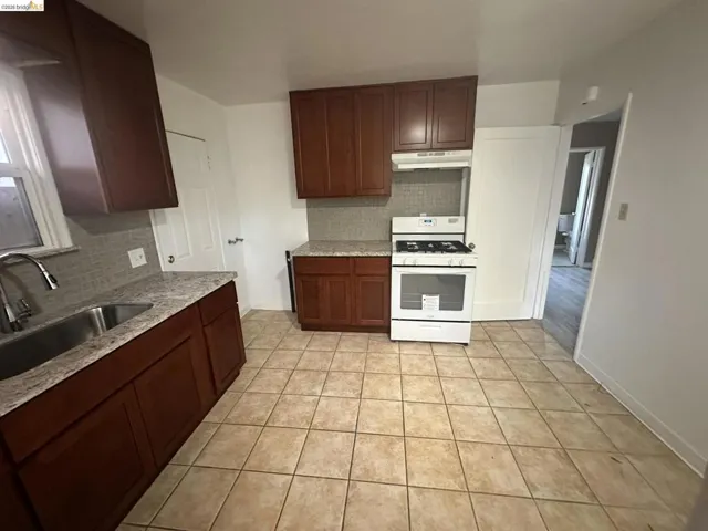 Kitchen featuring backsplash, white range with gas cooktop, light stone countertops, light tile patterned flooring, and dark wood finish cabinetry
