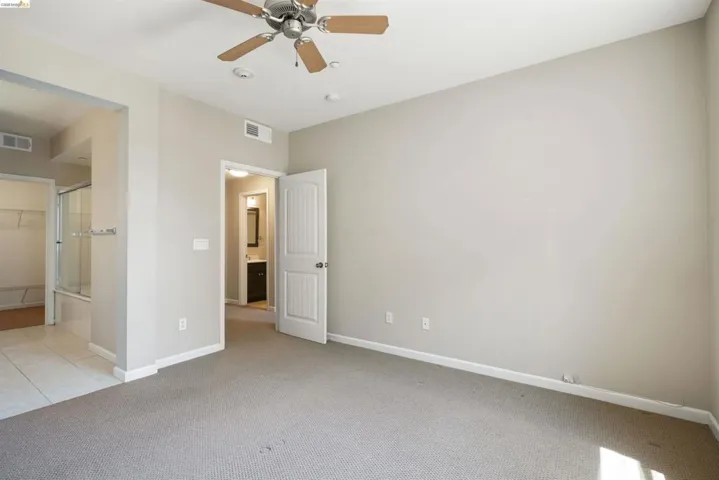 Unfurnished bedroom featuring light carpet, ensuite bath, a ceiling fan, and light tile patterned flooring