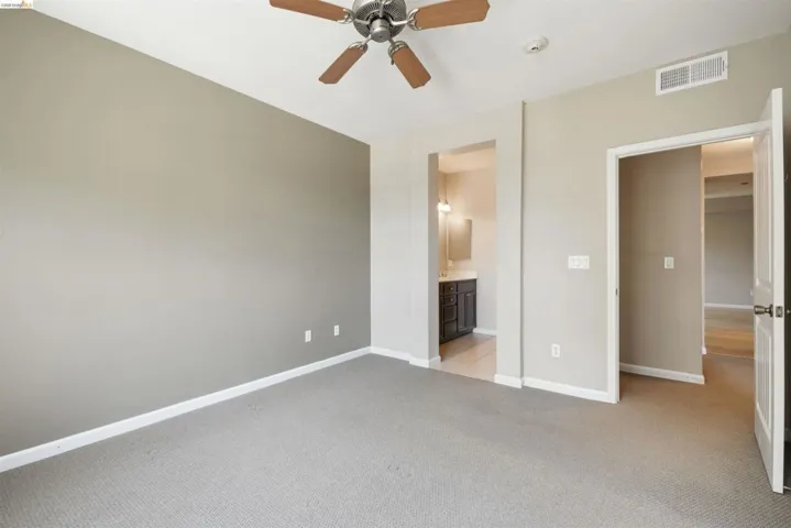 Unfurnished bedroom with light carpet, connected bathroom, and ceiling fan