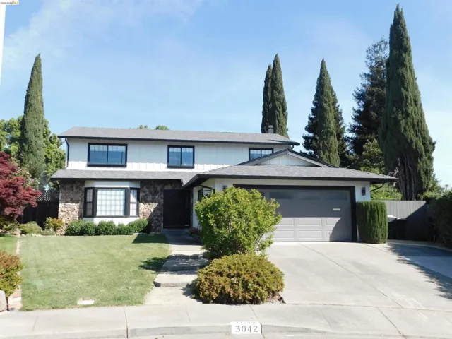 View of front facade featuring a garage, concrete driveway, stone siding, and a shingled roof