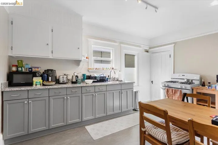 Dual tone kitchen with two tone cabinetry, white gas stove, black microwave, light stone counters, and dark wood-style floors