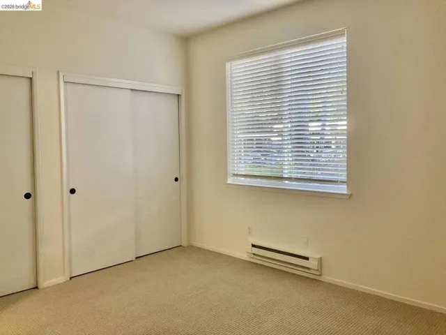 Unfurnished bedroom featuring multiple closets, light carpet, and baseboard heating