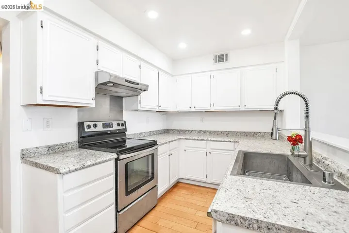 Kitchen featuring stainless steel electric stove, white cabinets, light wood-style floors, and recessed lighting