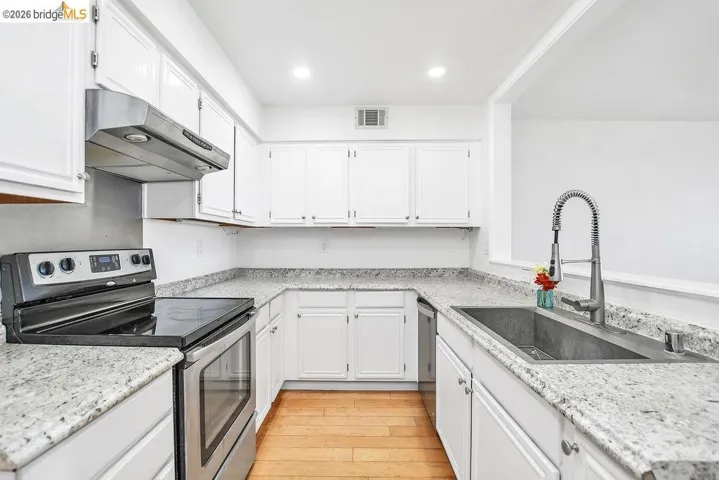 Kitchen with stainless steel appliances, white cabinets, light wood-type flooring, light stone counters, and recessed lighting