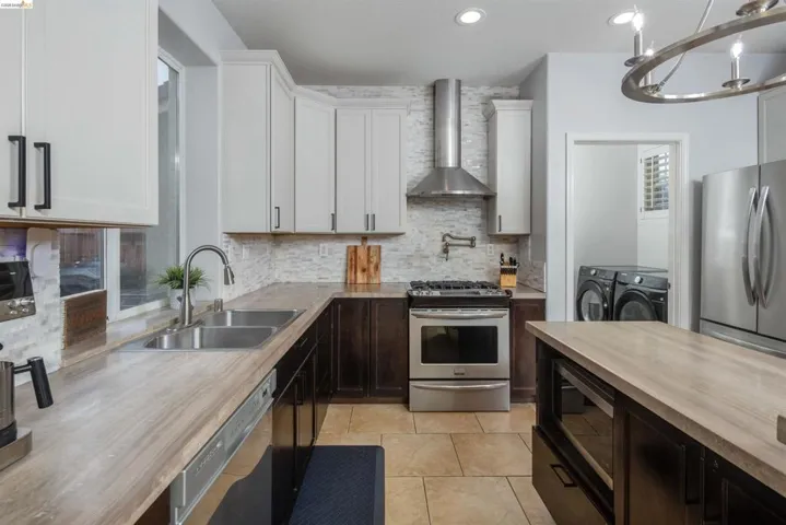 Kitchen featuring washing machine and clothes dryer, appliances with stainless steel finishes, wall chimney range hood, decorative backsplash, and butcher block countertops