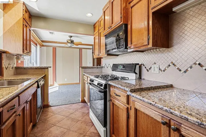 Kitchen featuring black appliances, backsplash, light stone counters, wood finish cabinets, and ceiling fan
