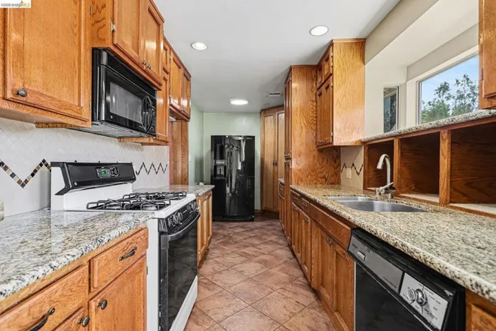 Kitchen featuring black appliances, backsplash, wood finish cabinetry, light stone countertops, and recessed lighting