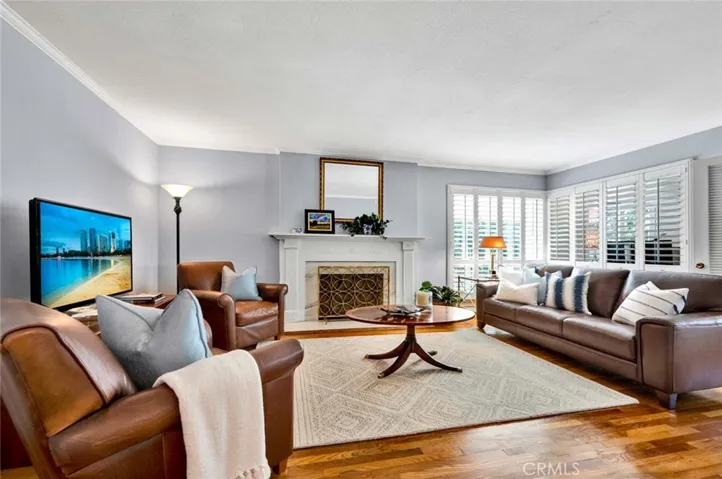 The living room features gleaming hardwood floors, a fireplace and plantation shutters.