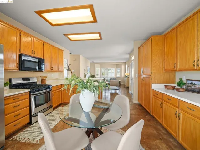Kitchen featuring stainless steel range with gas stovetop, light countertops, open floor plan, black microwave, and wood finish cabinetry