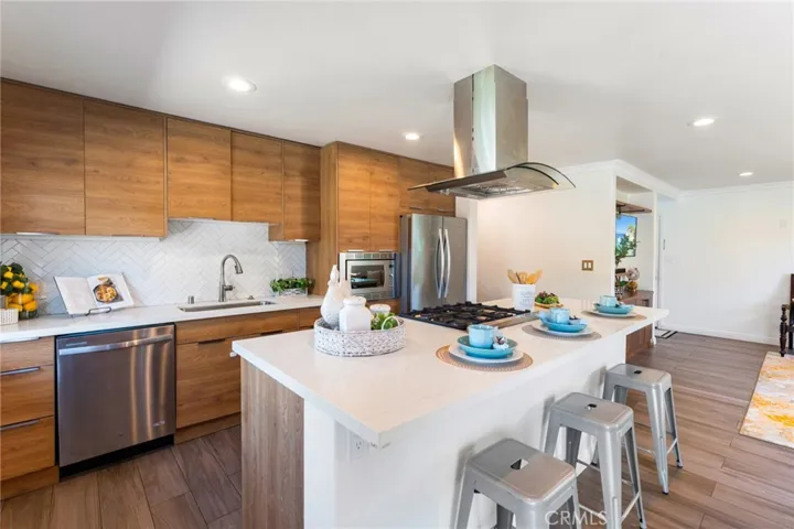 Quartz countertops, a large center island w/seating, honed herringbone mosaic tile backsplash, and sleek Euro-style soft-closing cabinetry with specialty storage and deep drawers. Premium stainless appliances include a Bertazzoni 5-burner range, Kobe vent hood, microwave, dishwasher, refrigerator, & a deep utility sink