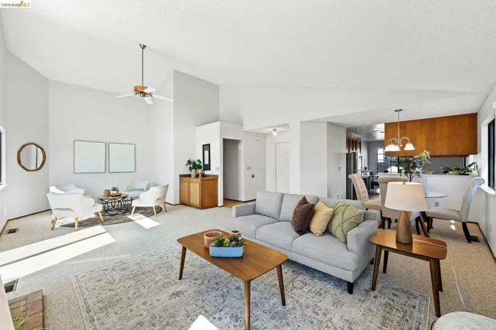 Living area featuring light colored carpet, ceiling fan, and vaulted ceiling