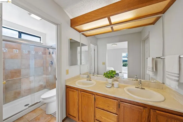 Bathroom featuring double vanity, healthy amount of natural light, a shower stall, light tile patterned floors, and a textured ceiling