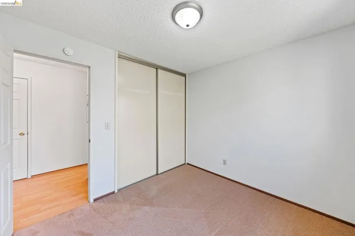 Unfurnished bedroom with a textured ceiling, light carpet, and a closet