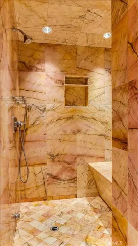 The marble shower has a bench and mulitple shower heads.