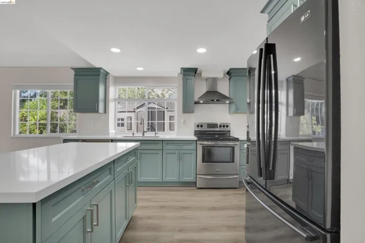 Kitchen featuring freestanding refrigerator, stainless steel electric range oven, light wood finished floors, recessed lighting, and green cabinetry