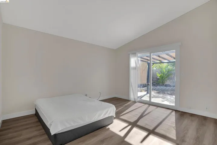 Bedroom with wood finished floors, access to outside, and vaulted ceiling