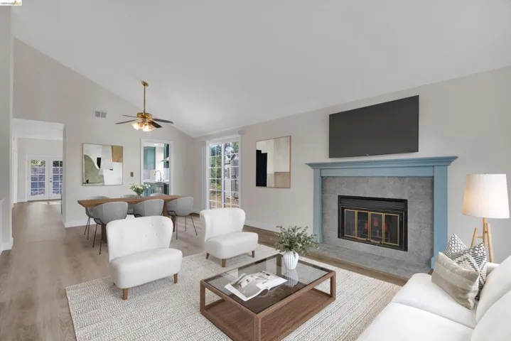Living room with wood finished floors, vaulted ceiling, a ceiling fan, and a tiled fireplace