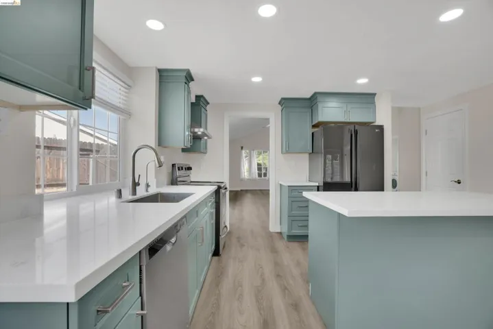 Kitchen with green cabinetry, stainless steel appliances, recessed lighting, light wood-style floors, and light stone counters