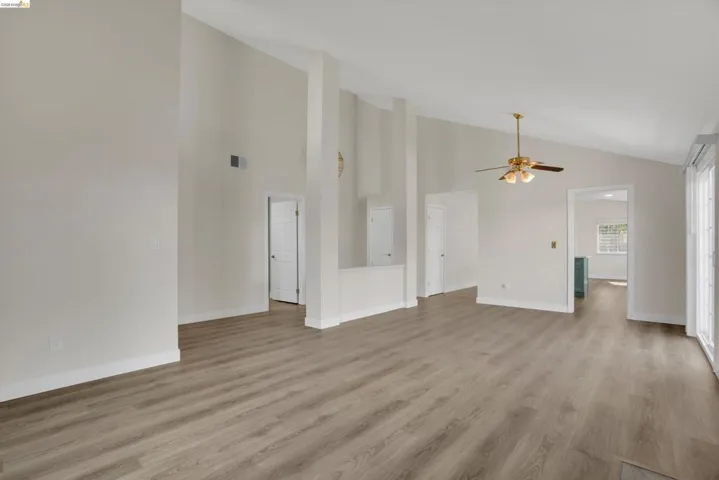 Unfurnished living room featuring a ceiling fan, light wood-style flooring, and lofted ceiling