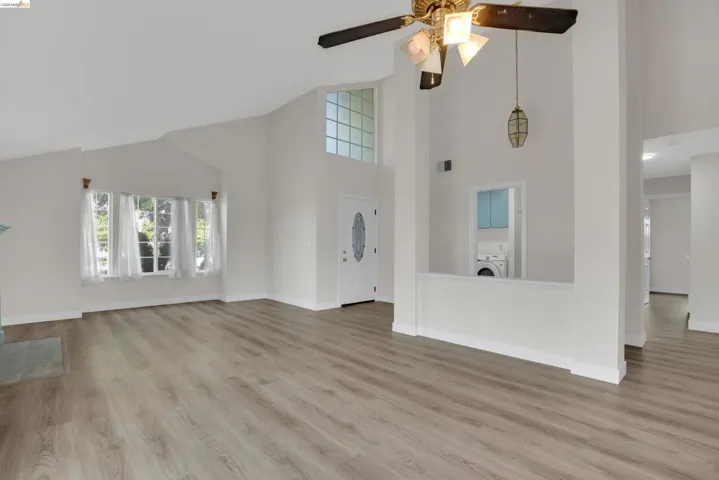 Unfurnished living room with light wood finished floors, ceiling fan, vaulted ceiling, and washer / dryer
