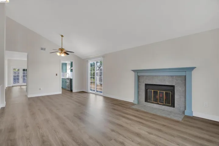 Unfurnished living room with light wood-style flooring, lofted ceiling, a ceiling fan, and a tile fireplace