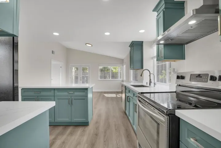 Kitchen with stainless steel electric stove, green cabinetry, vaulted ceiling, light wood-style floors, and light stone counters