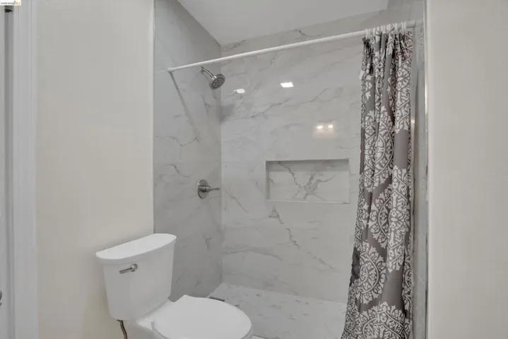 Full bath featuring toilet and a marble finish shower