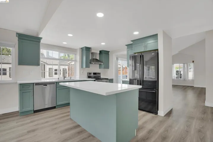 Kitchen with green cabinets, stainless steel appliances, a kitchen island, light wood-style flooring, and recessed lighting