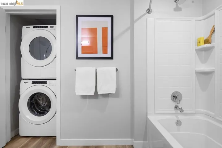Full bathroom with washtub / shower combination, stacked washing machine and dryer, and wood finished floors