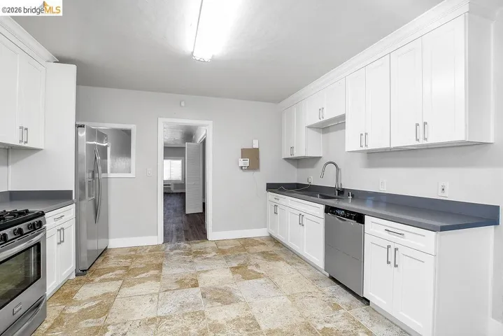 Kitchen with stainless steel appliances, white cabinetry, and dark countertops