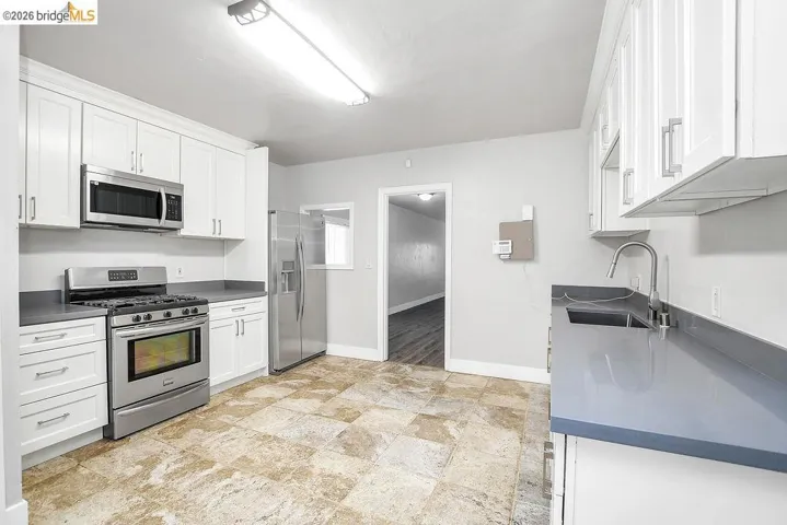 Kitchen featuring stainless steel appliances, dark countertops, and white cabinetry