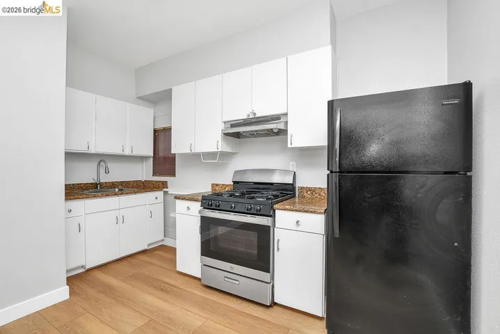 Kitchen featuring freestanding refrigerator, stainless steel gas range, white cabinetry, and light wood-style flooring