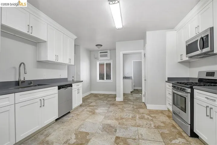 Kitchen featuring stainless steel appliances, dark countertops, and white cabinetry