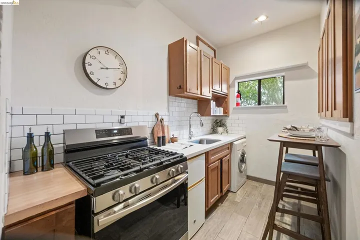 Kitchen featuring stainless steel range with gas cooktop, wood finish cabinets, washer / clothes dryer, light wood-type flooring, and backsplash