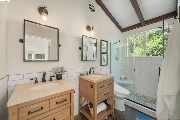 Bathroom with tile walls, two vanities, a stall shower, a wainscoted wall, and lofted ceiling