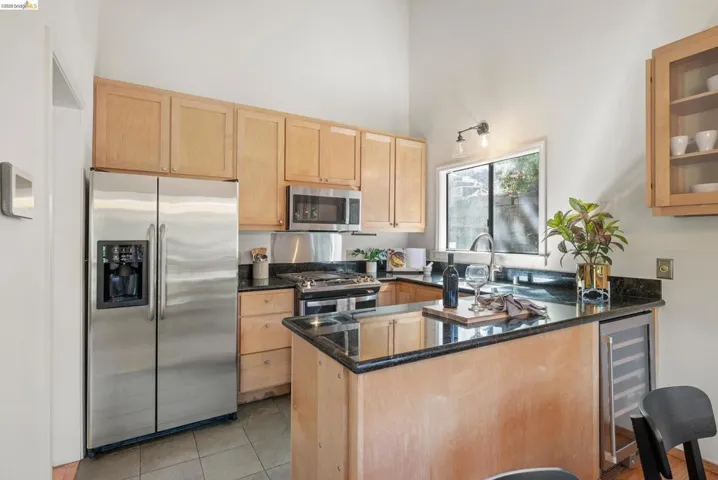 Kitchen with stainless steel appliances, dark stone countertops, a peninsula, light wood finish cabinets, and beverage cooler