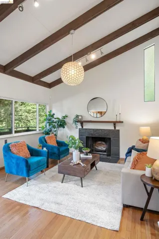 Living room featuring a tiled fireplace, light wood-style flooring, and lofted ceiling with beams