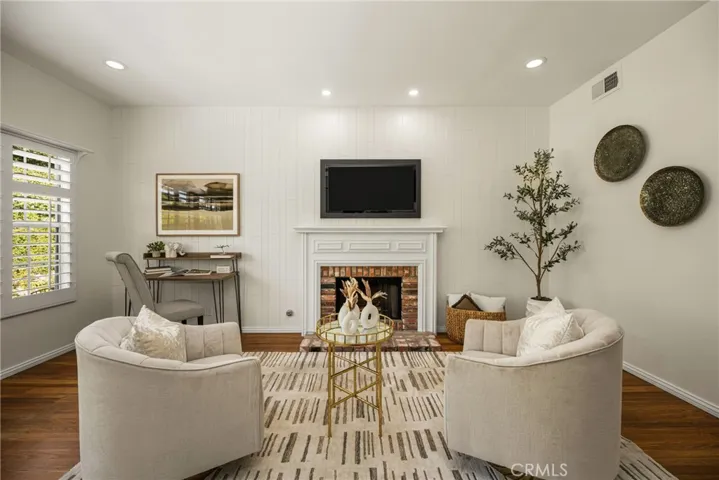 Retreat area in the primary suite features hardwood flooring, plantation shutters, recessed lighting, wood paneling  and a fireplace with custom wood surround.