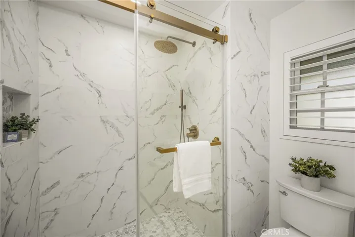 Remodeled primary shower features tile surround, sleek gold fixtures with a glass barndoor enclosure.