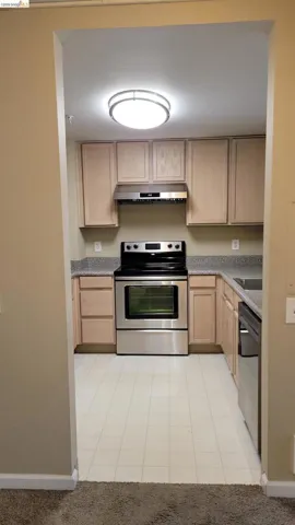 Kitchen with light wood finish cabinetry, stainless steel electric range, black dishwasher, and light tile patterned floors