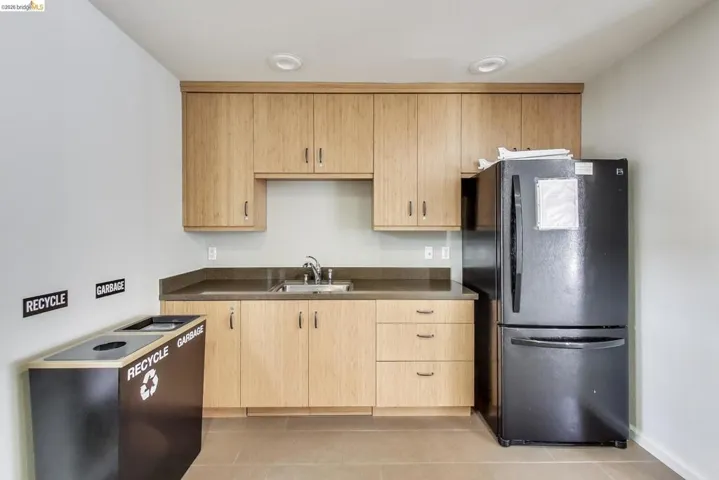 Kitchen featuring dark countertops, freestanding refrigerator, light wood finish cabinets, and light tile patterned flooring
