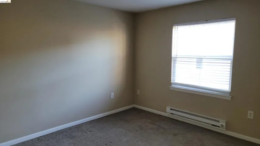 Carpeted empty room with a baseboard radiator and baseboards