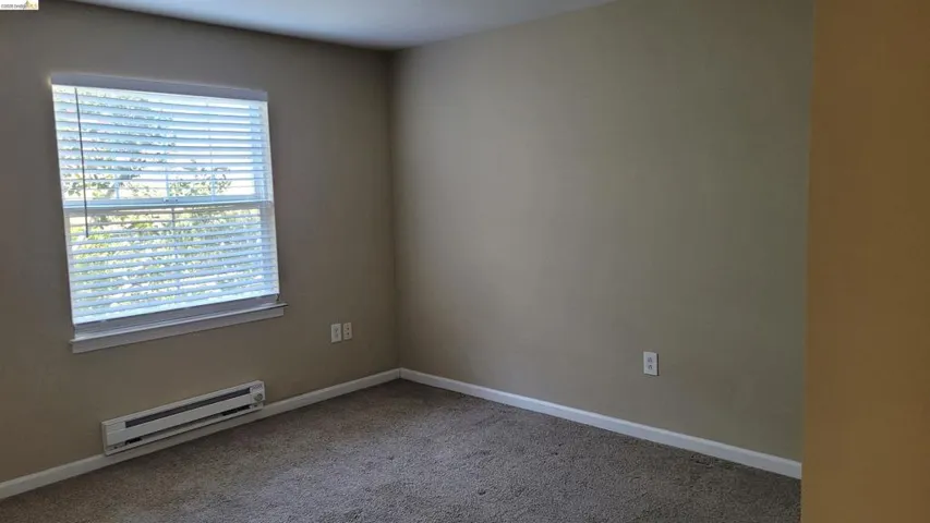 Unfurnished room featuring a baseboard heating unit and light carpet