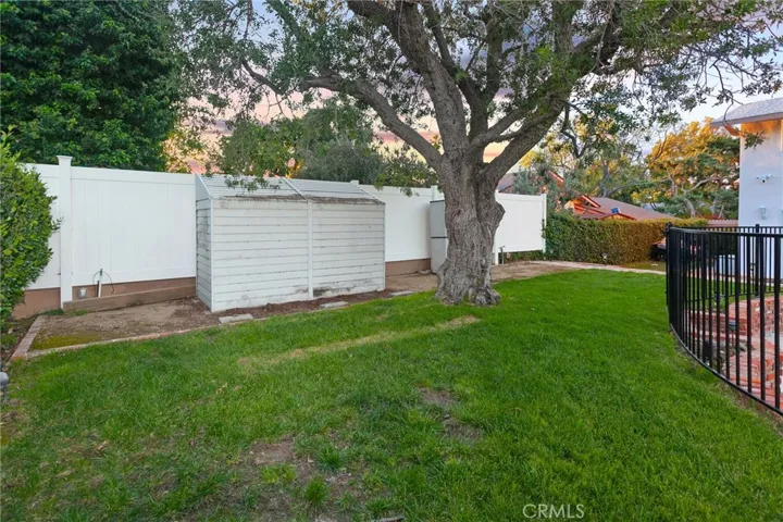 The backyard offers a private and inviting setting designed for relaxation and enjoyment, featuring a fenced in-ground pool and spa, covered and open patio areas, a grassy lawn, and raised brick planters with roses. A mature shade tree, outdoor lighting, and a garden shed enhance the space, while the side yard with artificial grass and a mini putting green adds a fun and functional touch.